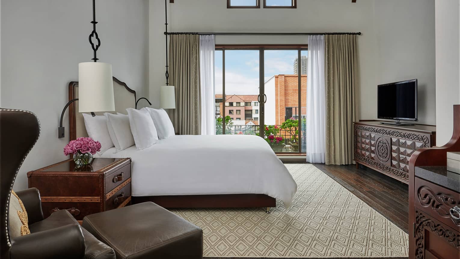 Superior room leather armchair, ottoman, trunk-style nightstand, hanging white lamps, bed by balcony door