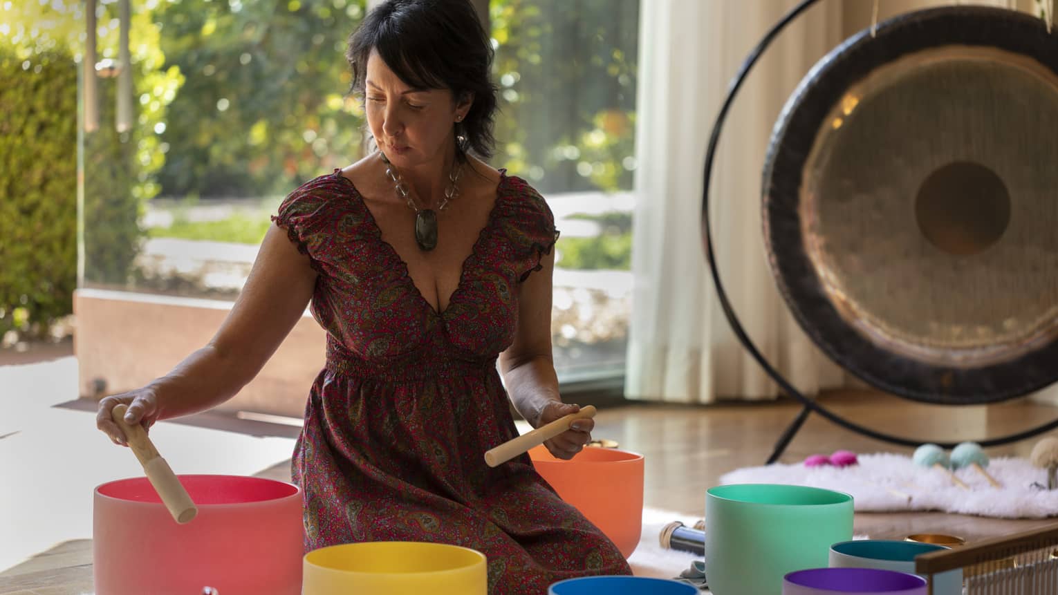 A woman conducting sound therapy using coloured bowls in an outdoor setting.