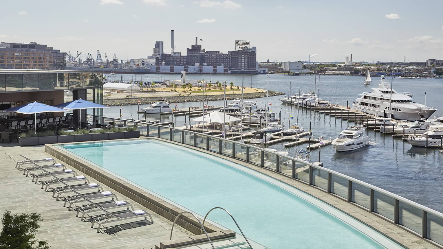 View over large outdoor swimming pool on patio by harbour with boats