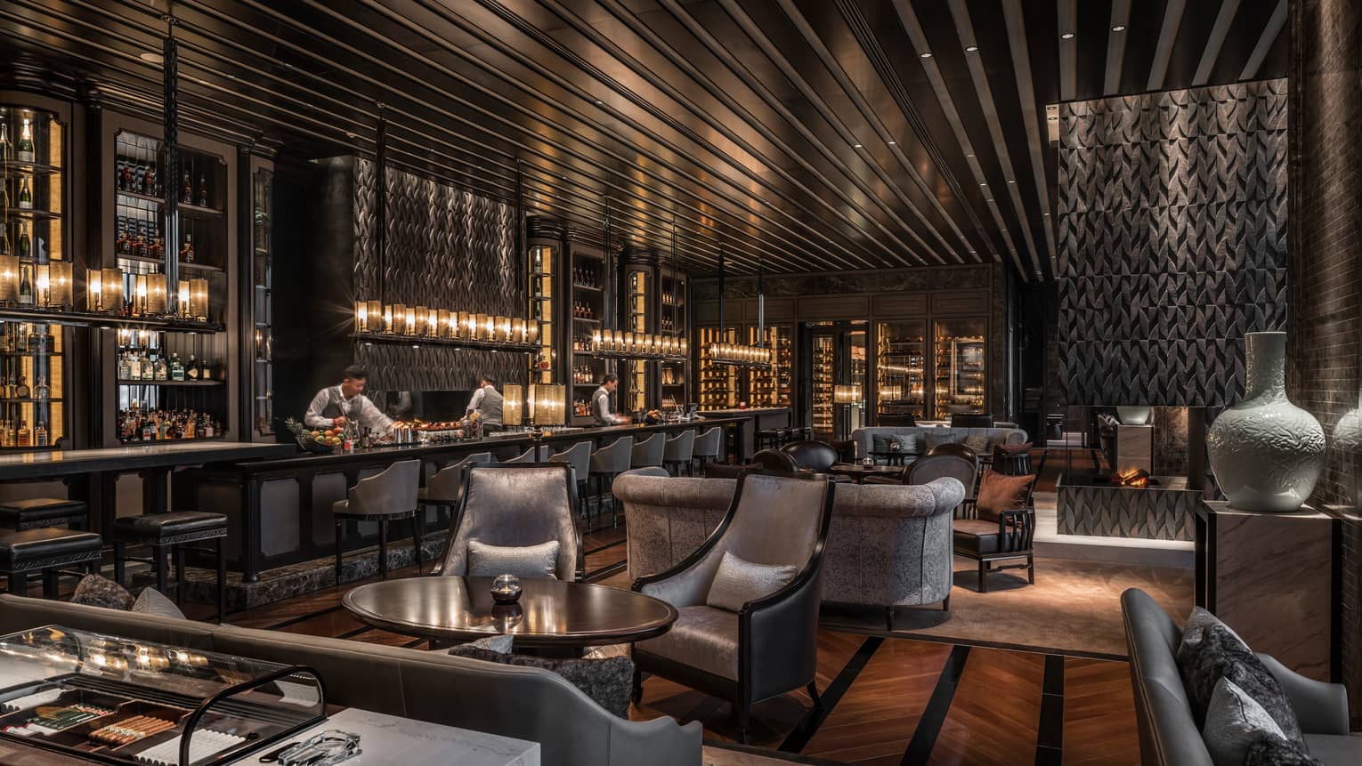 Gusto Bar bartenders at long bar lined with silver stools, grey velvet sofas, chairs
