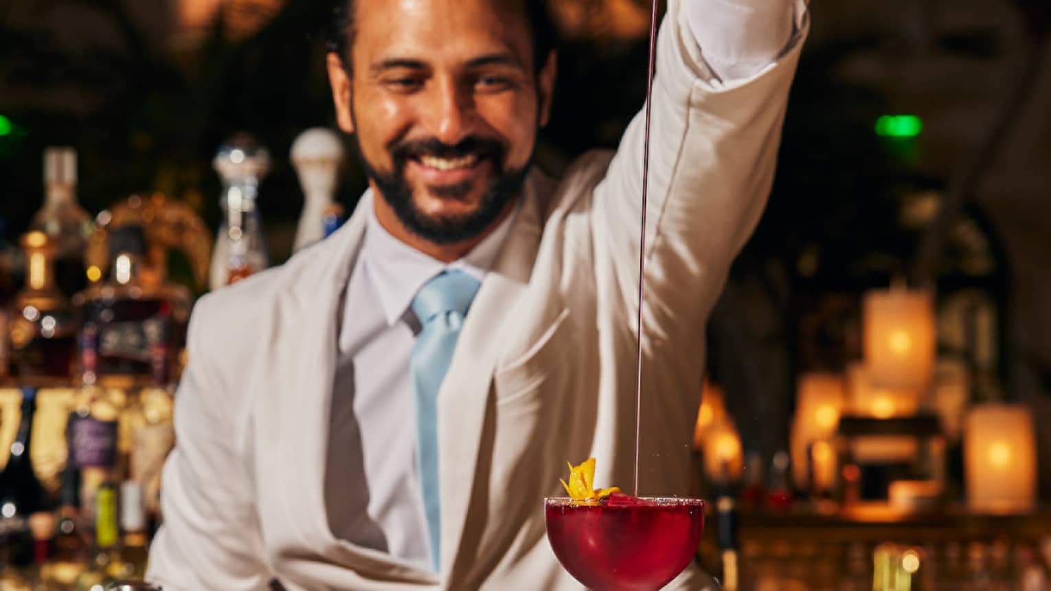 Bartender pours a cocktail from a silver cocktail shaker into a glass
