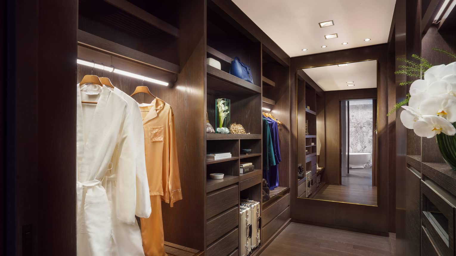 Large walk-in closet with built-in shelving, dark wood floors, floor length mirror