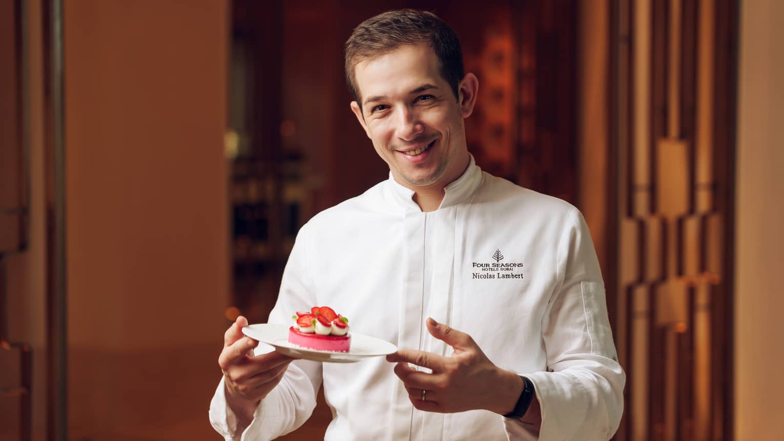Chef Nicolas Lambert wears a white chef's jacket and holds a plate of dessert