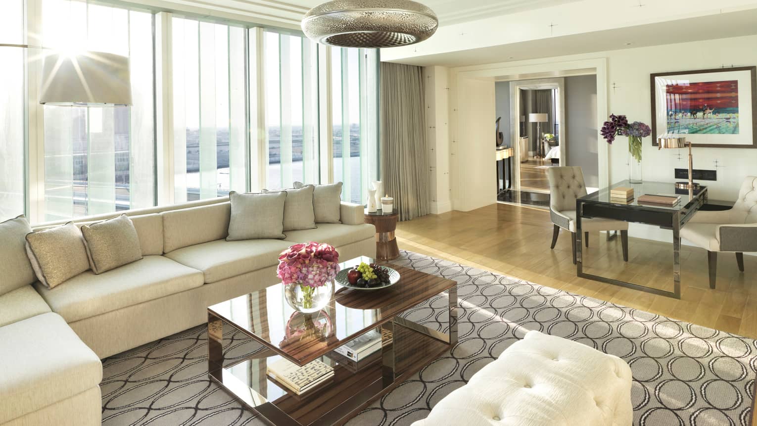 Deluxe Four Seasons Executive Suite living room with L-shaped white sofa, bench against bright window, dining table