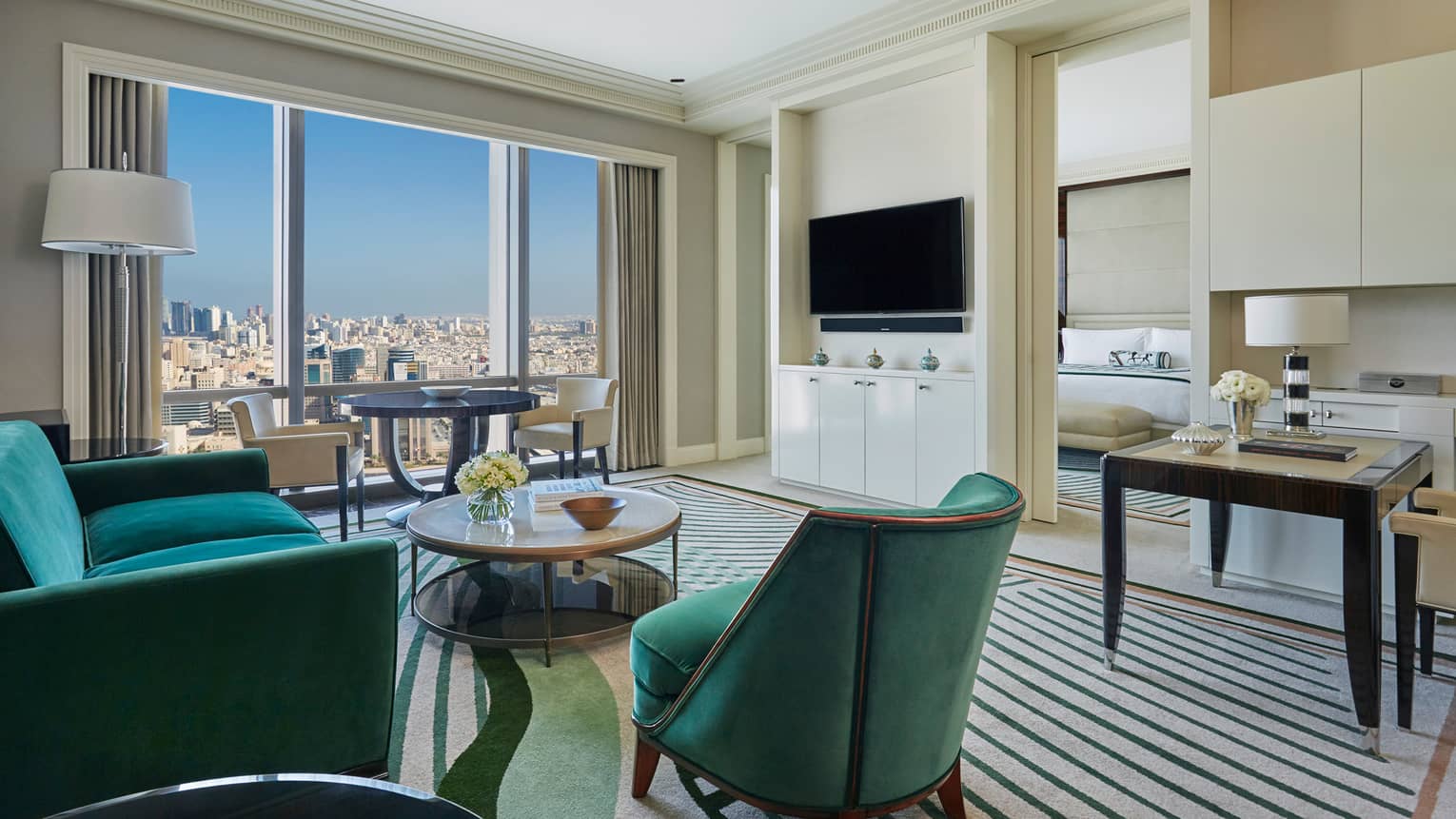 Four Seasons Deluxe Suite maritime green velvet armchair, sofa facing wall with TV, door to bedroom