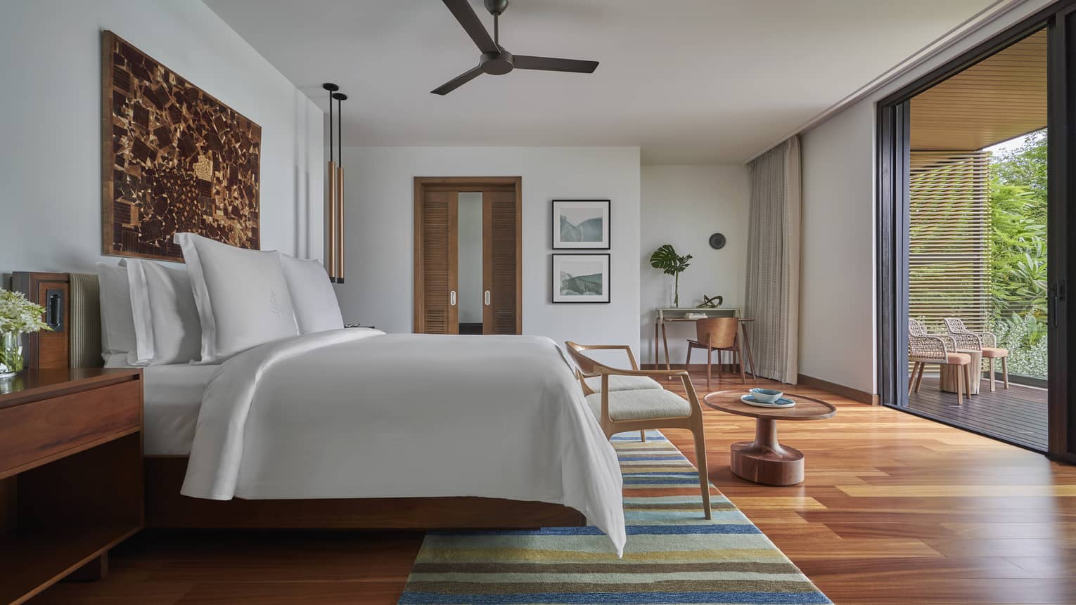 Bedroom with wooden floors, colourful area rug, king bed and private wooden terrace