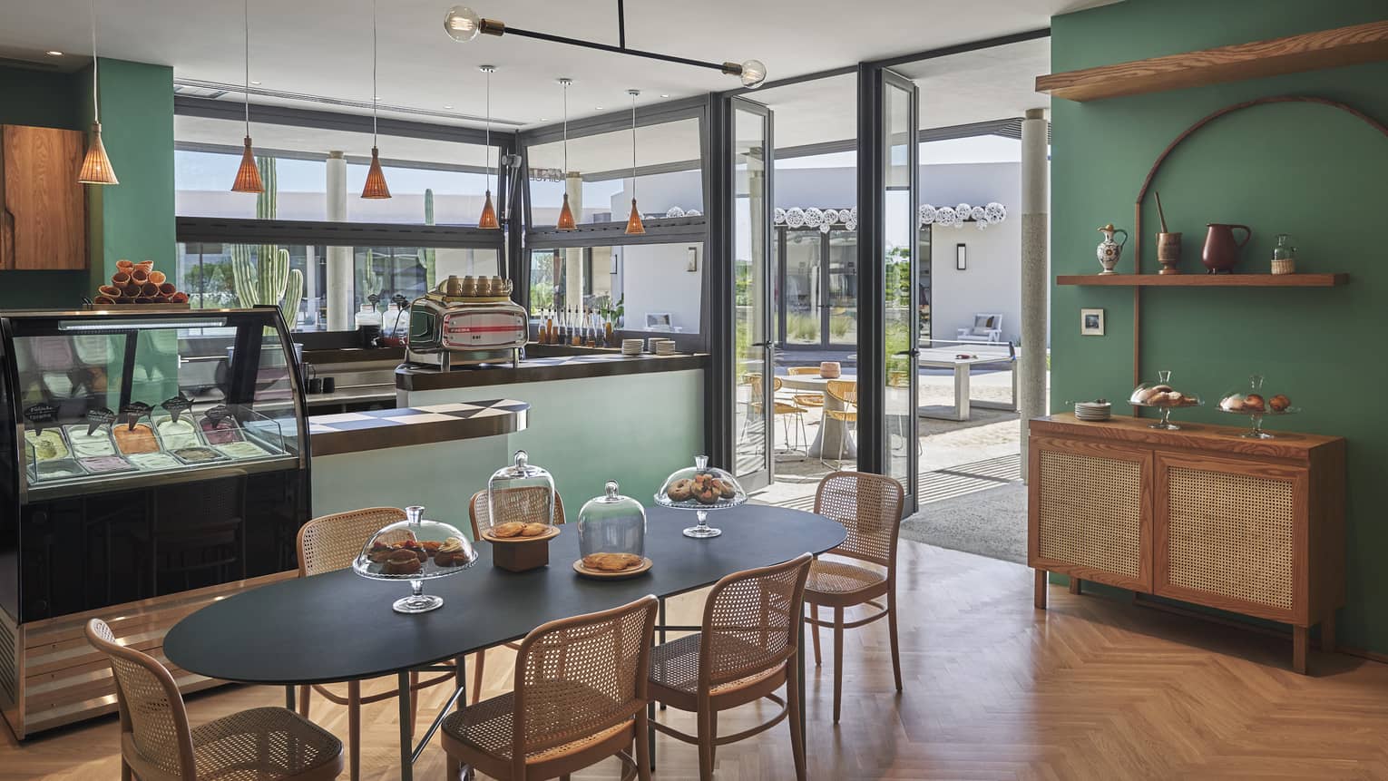 Green-walled Gingers dining area, black oval table and wicker chairs, food display case