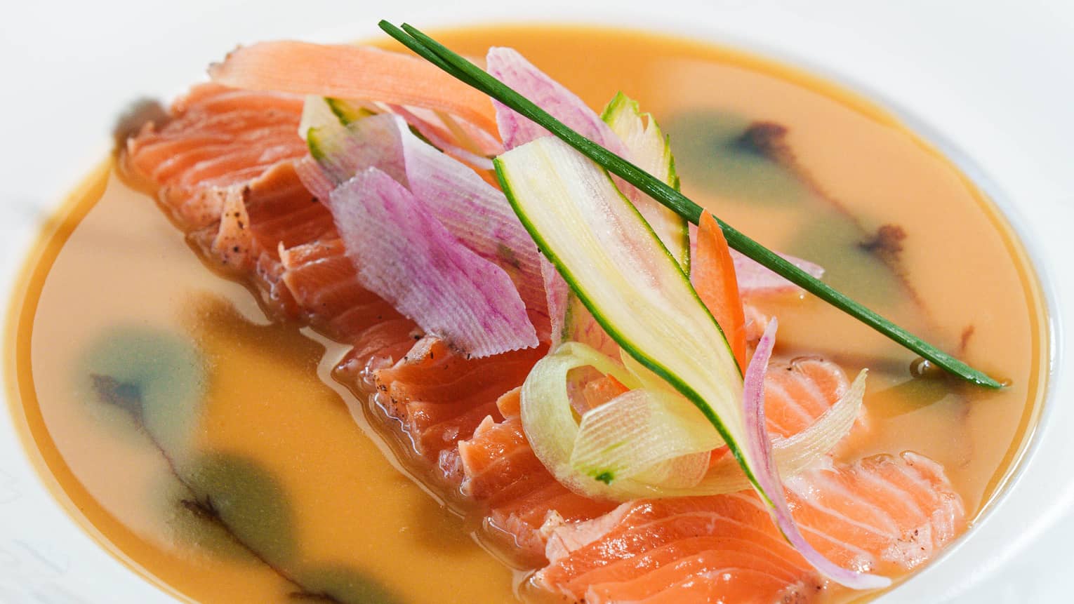 White bowl of salmon slices garnished with shaved vegetables