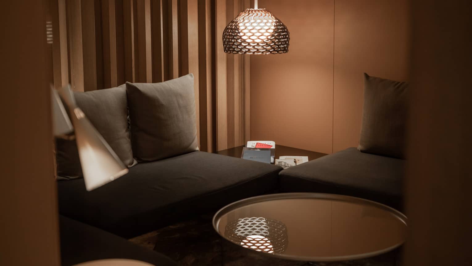 Corner of a modern spa lounge area with black couches, a circular, mirror-top coffee table and floor lamp