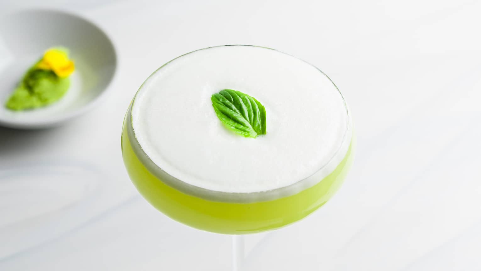 Light Green Wasabi Martini with foamy top and mint garnish in saucer champagne glass