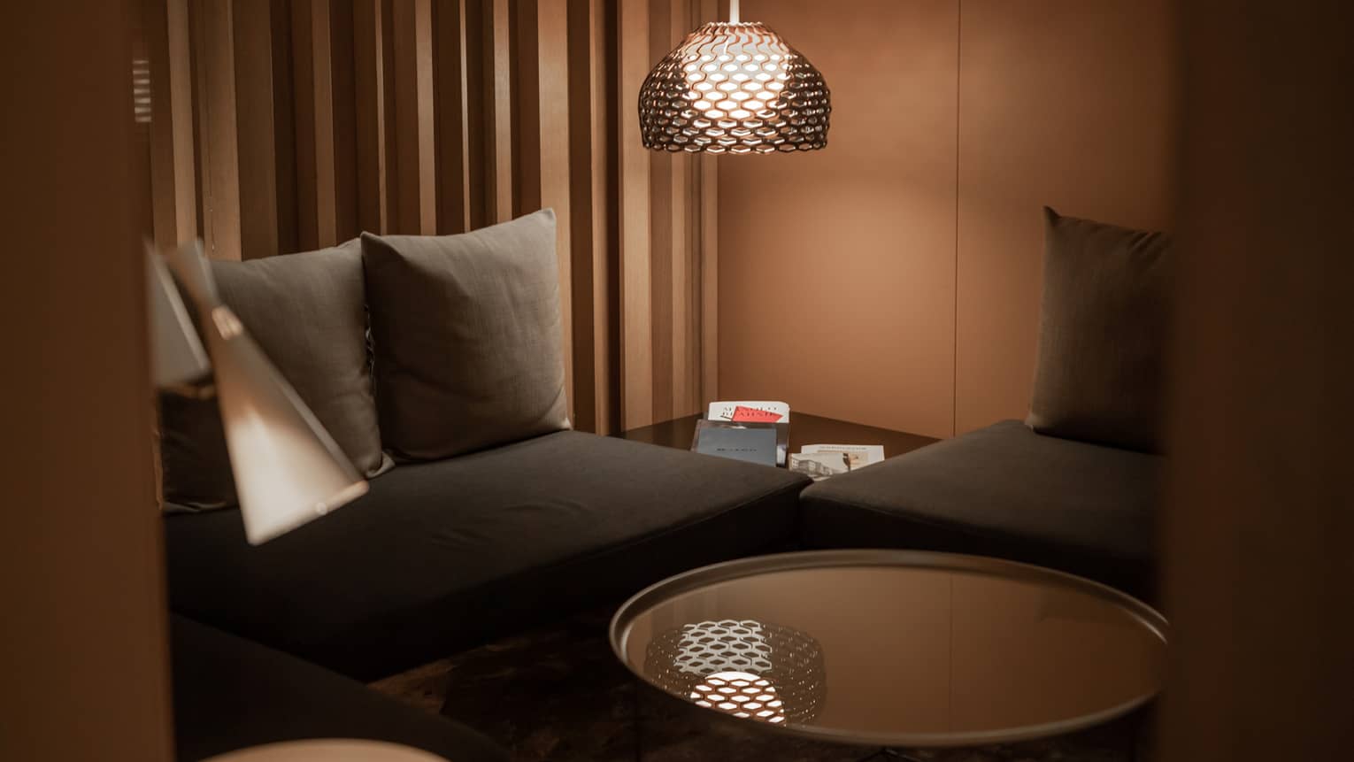 Corner of a modern spa lounge area with black couches, a circular, mirror-top coffee table and floor lamp