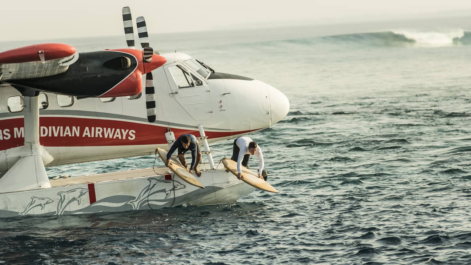Two people with surfboards jump from float plane onto waves