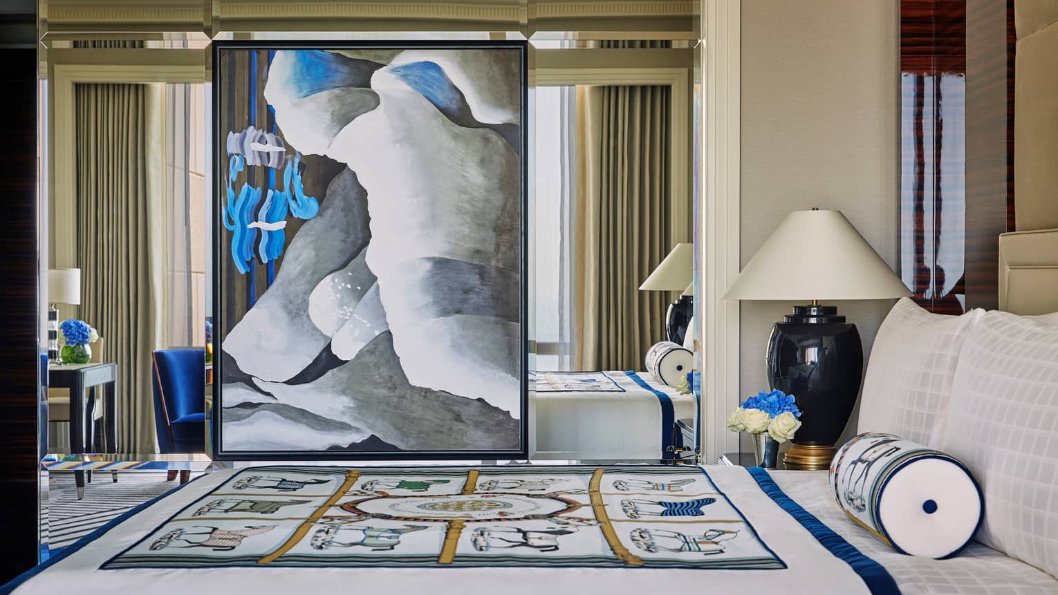 Large modern painting hangs on mirror wall beside bed with decorative blanket