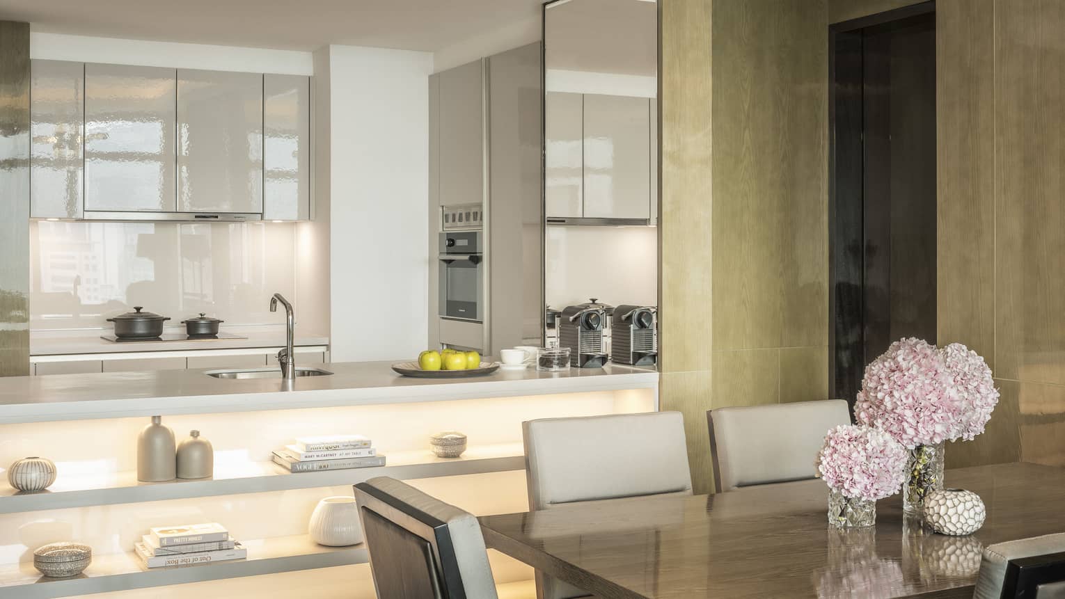 Dining table with flowers in front of open concept kitchen with accent shelf, white counter, cabinets