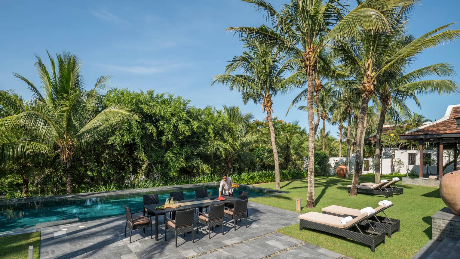 Server sets long patio dining table by Hilltop Villa outdoor swimming pool