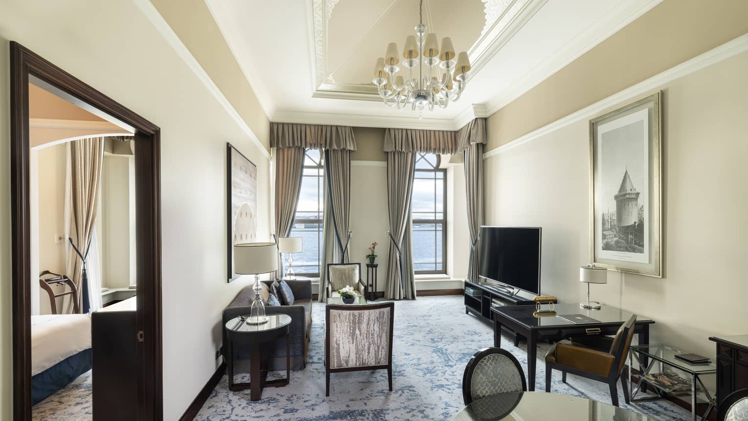 Elegant hotel suite living room featuring a chandelier, sofa, two chairs, TV and dining table