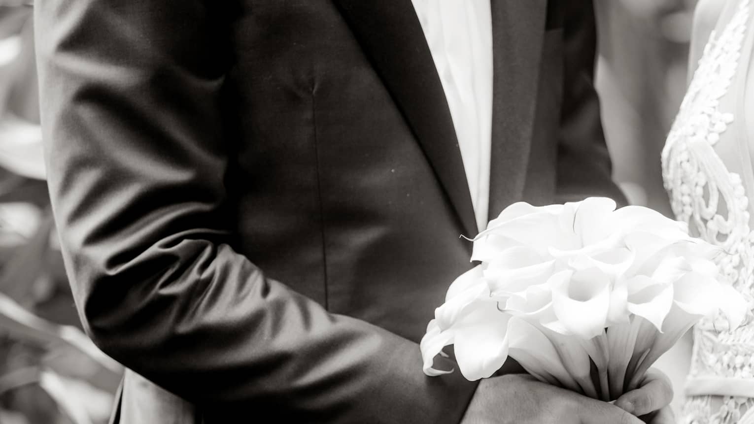 Black and white image of bride wearing lace dress, groom holding wedding bouquet