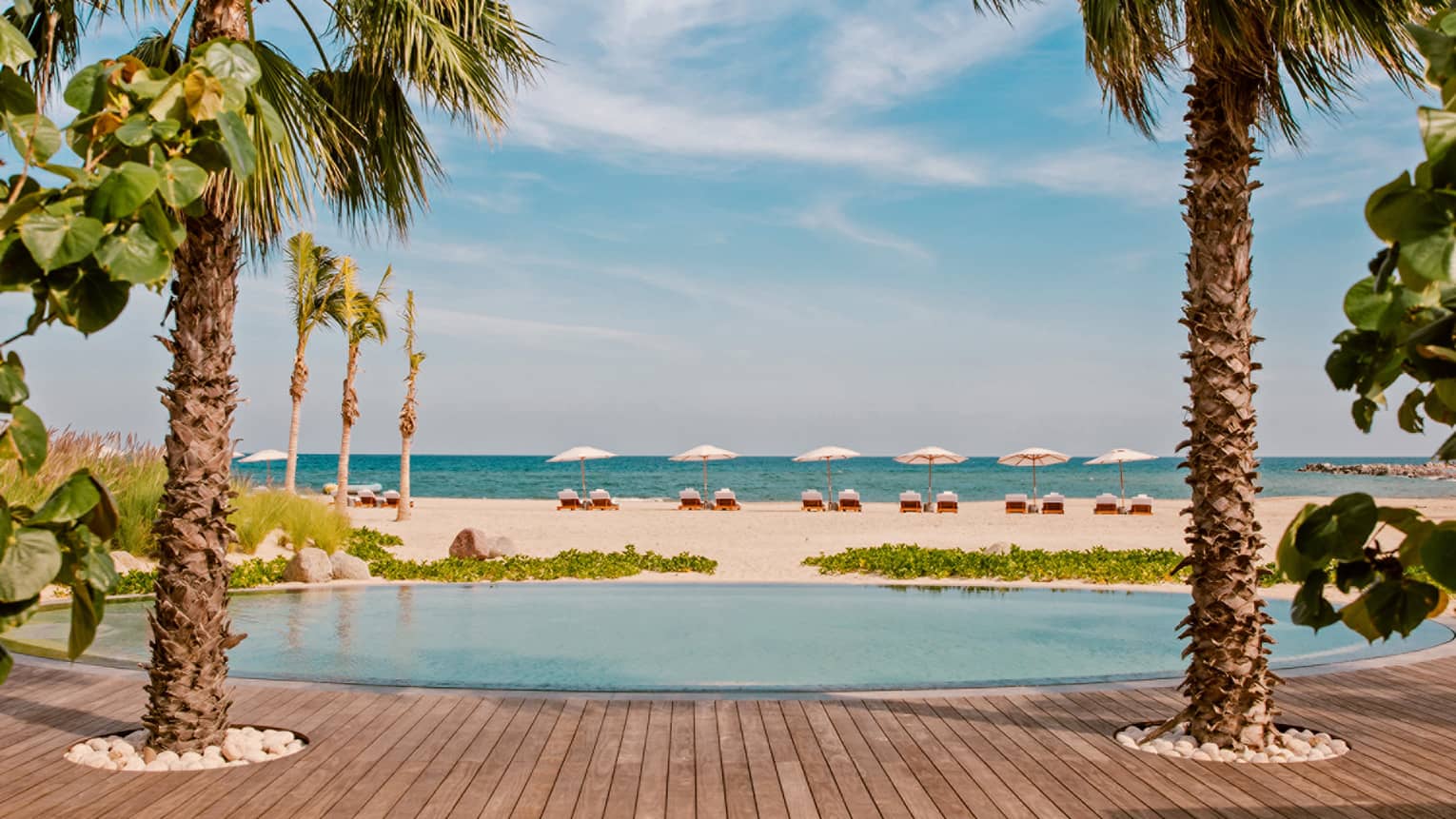 A round pool next to a white sand beach and palm trees.