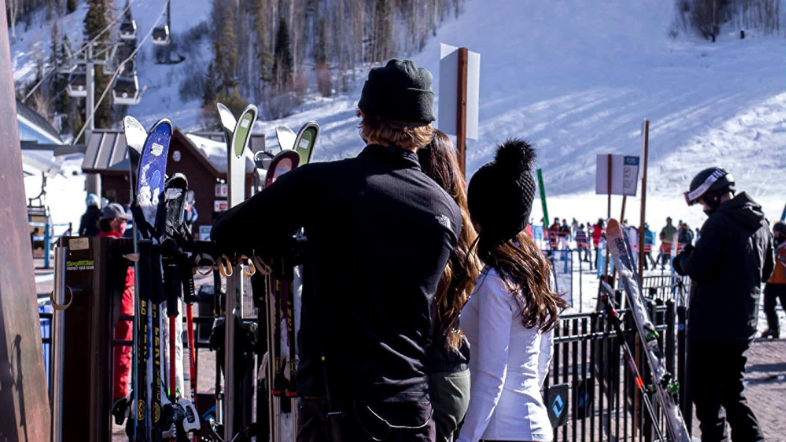 A group of people looking at skis and snowboards outside near a hill with snow on it.