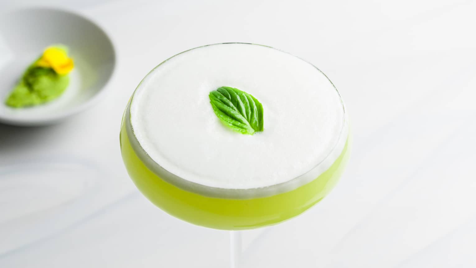 Light Green Wasabi Martini with foamy top and mint garnish in saucer champagne glass