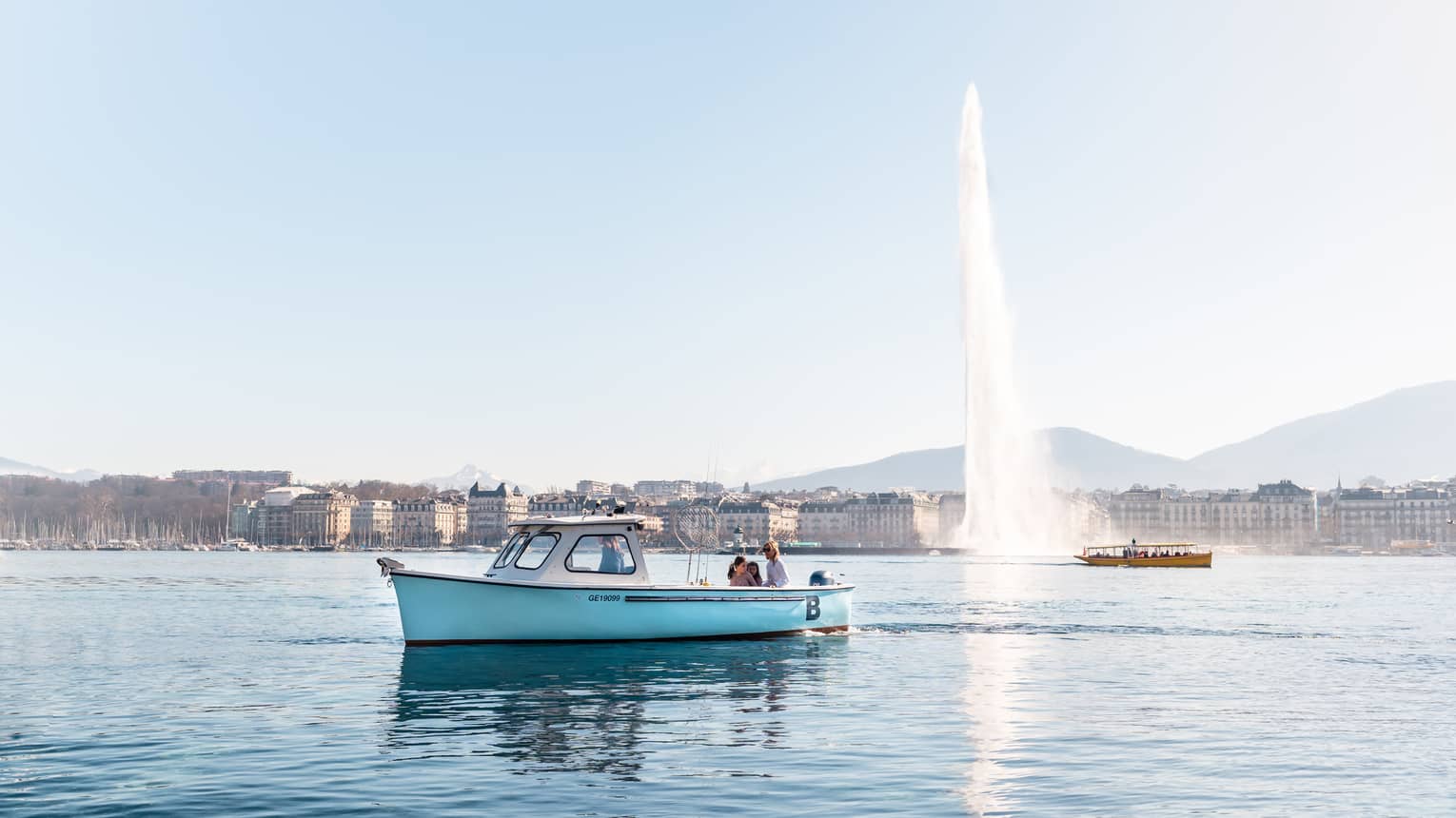 Small blue fishing boat on Lake Geneva in front of Jet d'Eau fountain