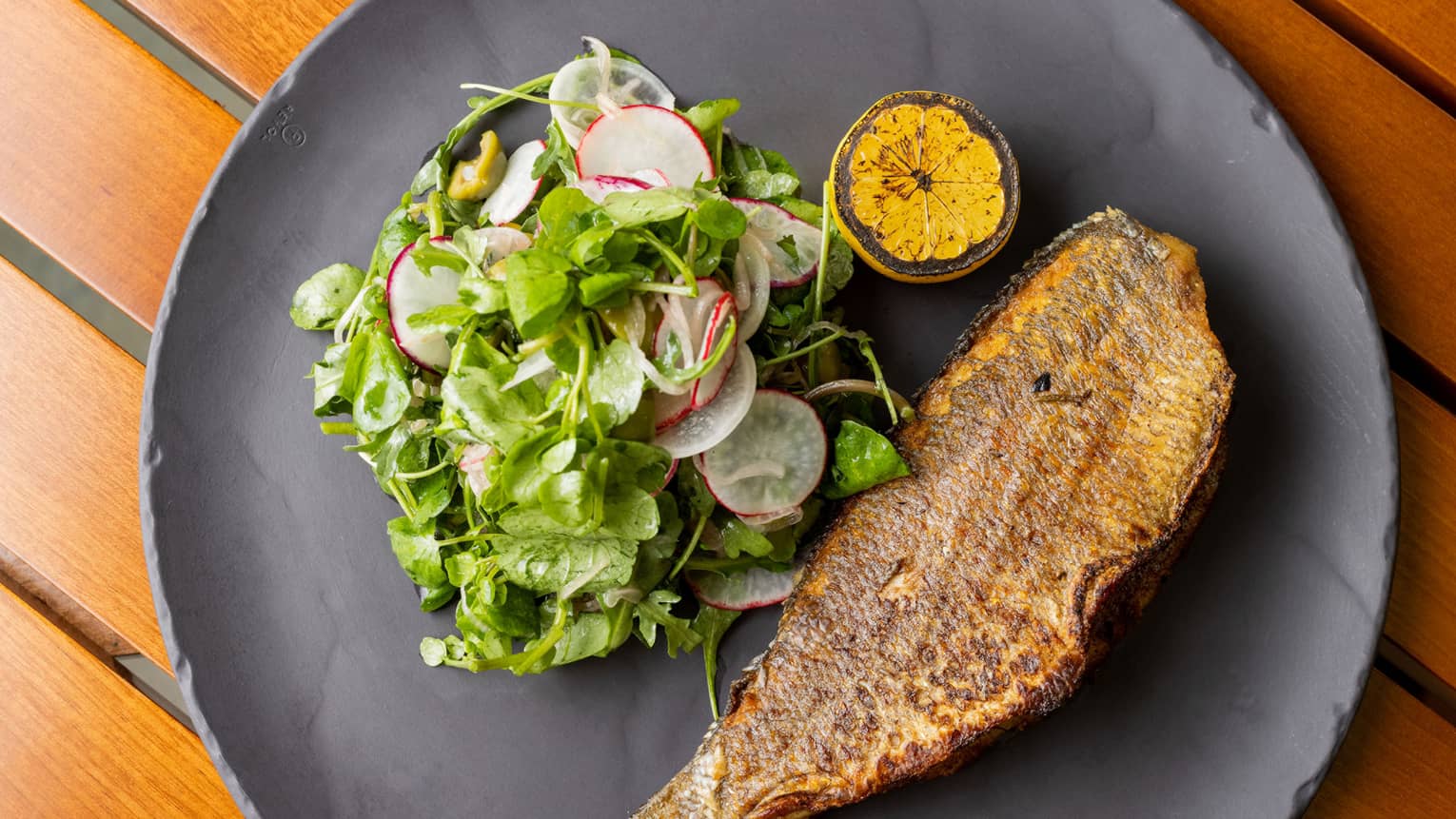 Cooked fish and a green salad on a grey plate.