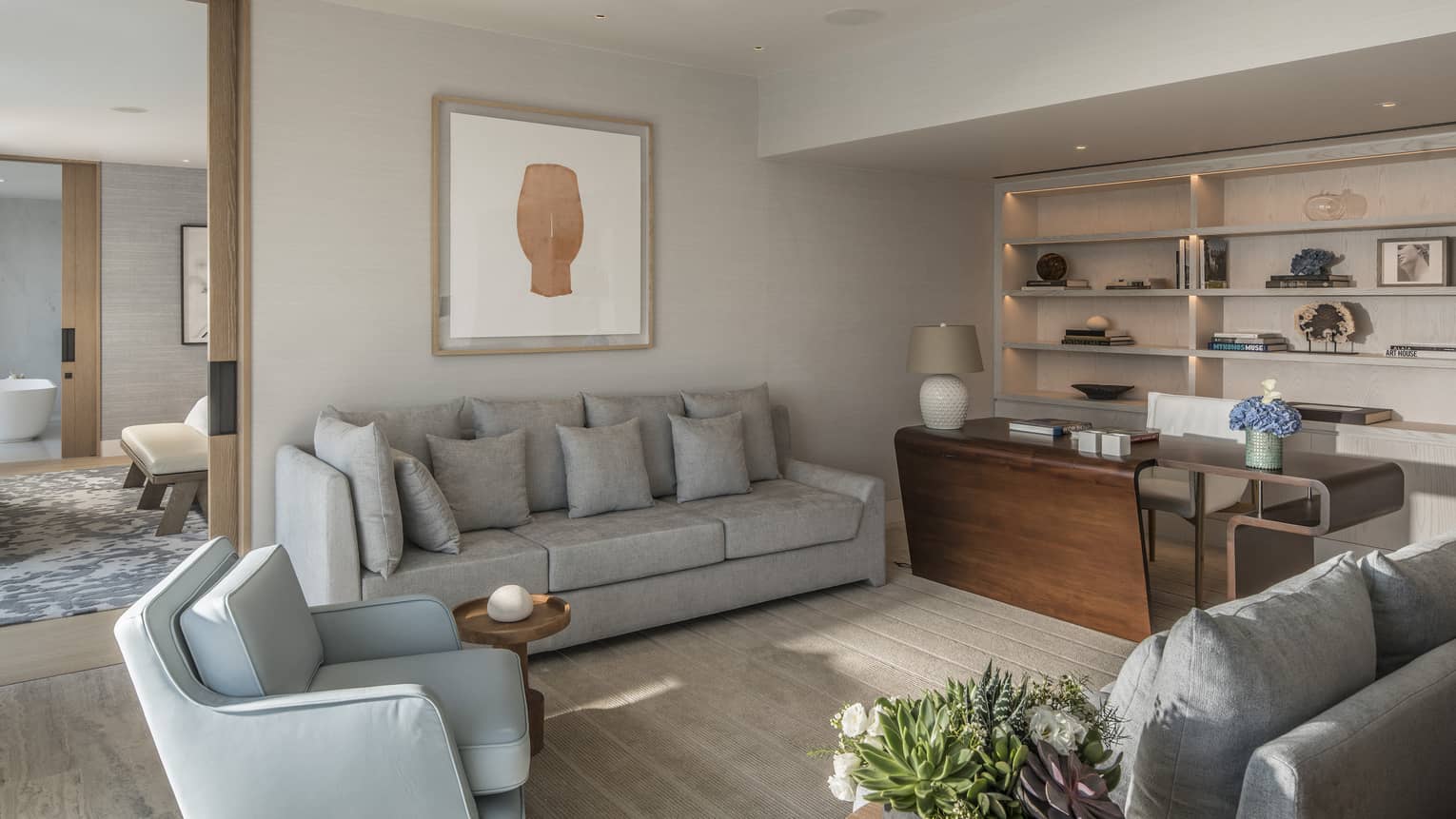 Arion Presidential Suite living area with grey sofa, armchair and loveseat; built-in backlit shelves, doorway to bedroom