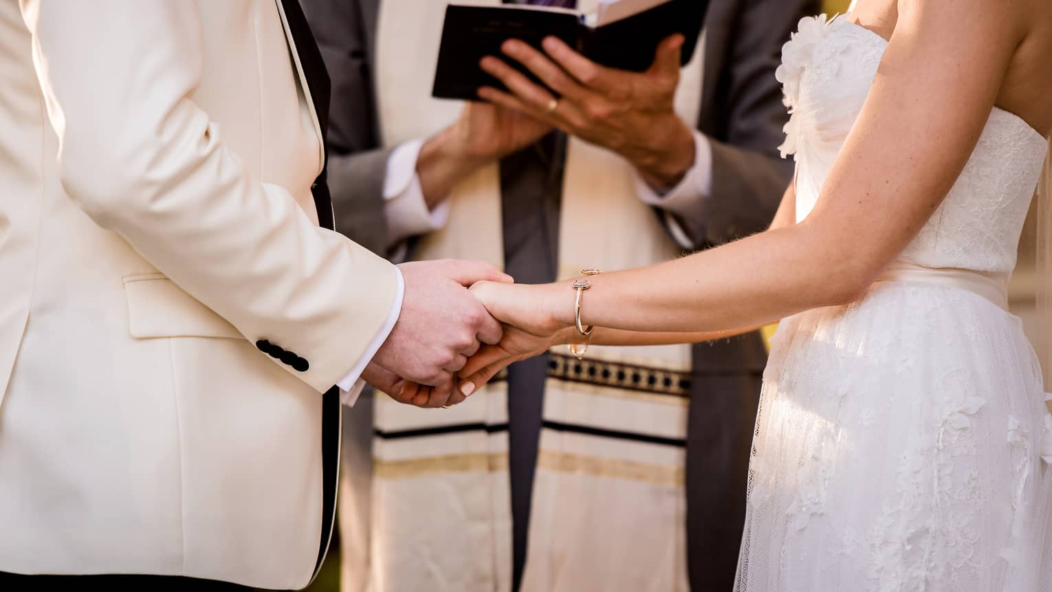 Bride and groom hold hands in front of wedding ceremony officiant