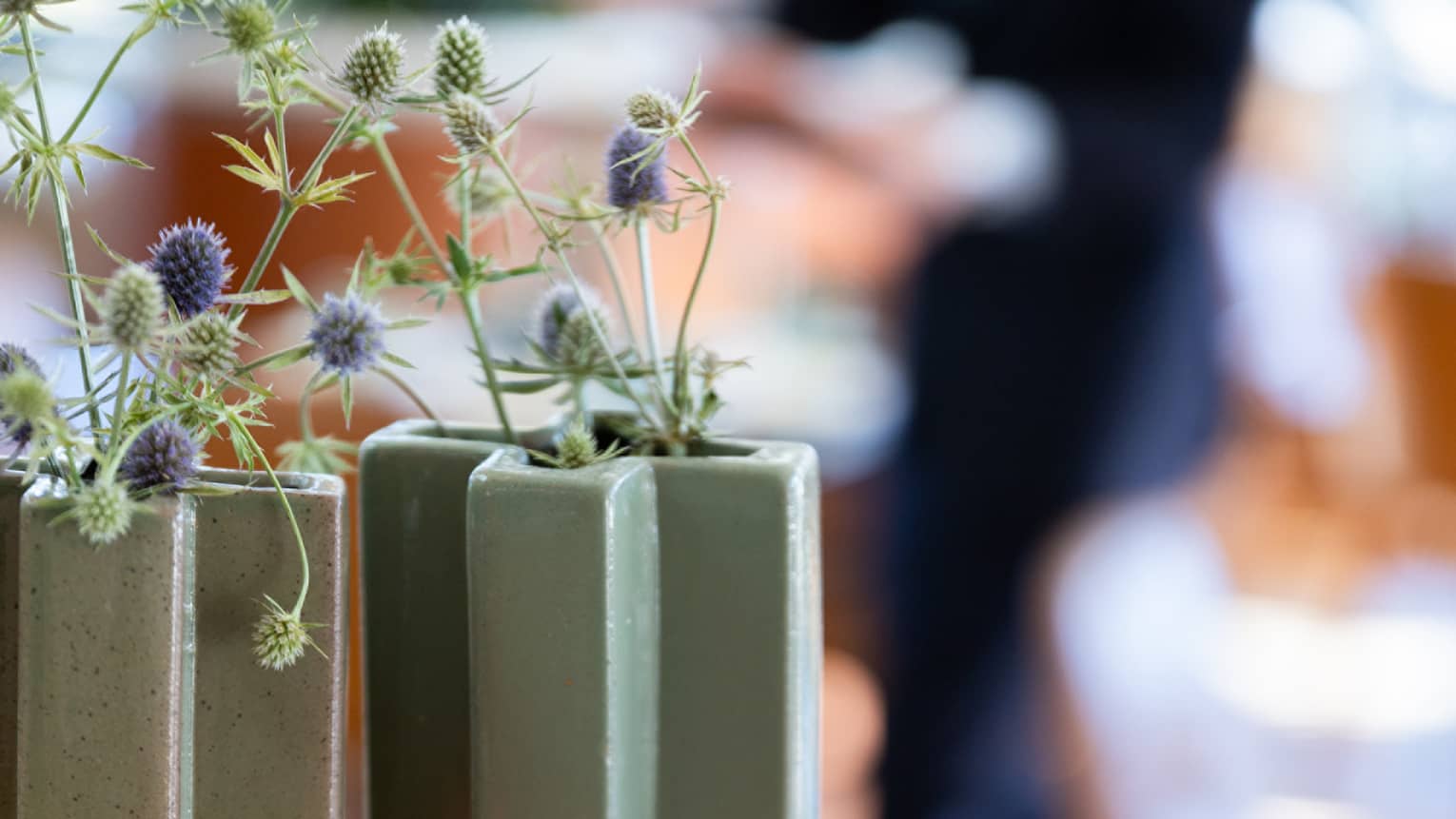 Purple and green flowers in slate-green vases sit on top of two books stacked on a marble table