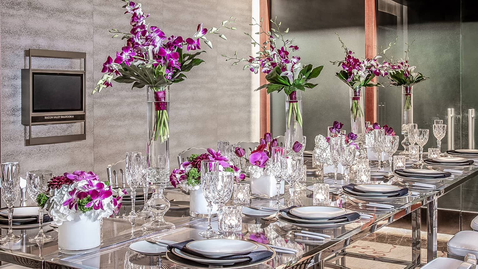 Purple flowers, goblets and place-settings decorate a glass able in an event space