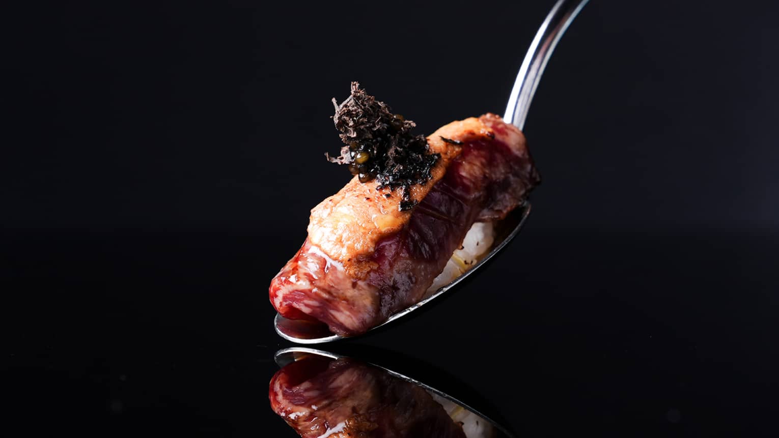 Spoon holding a piece of nigiri sushi on a black backdrop