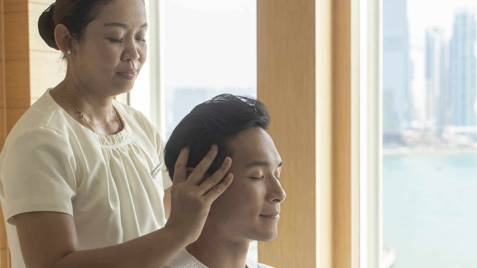 Female spa therapist massages a man's head
