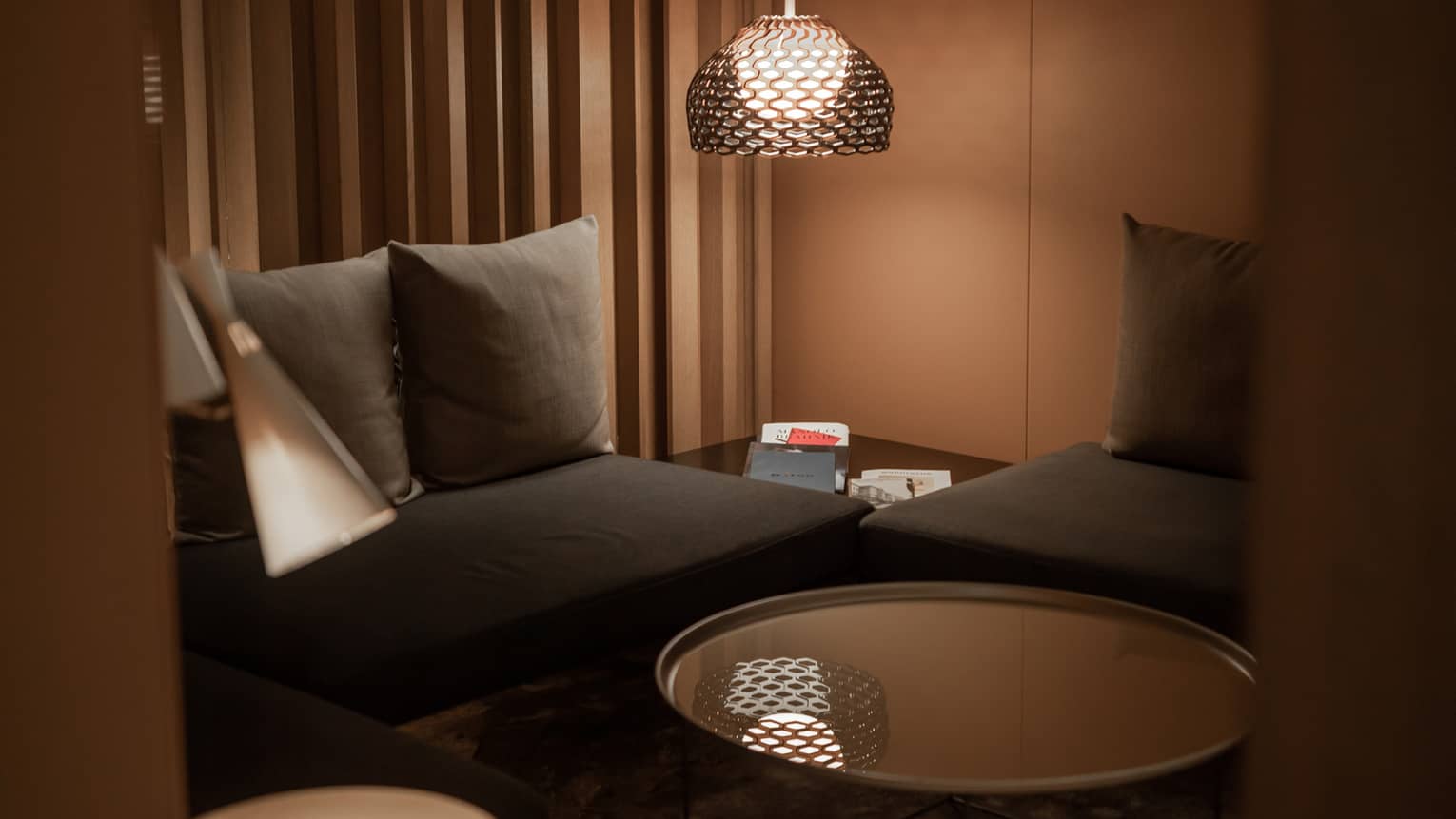 Corner of a modern spa lounge area with black couches, a circular, mirror-top coffee table and floor lamp