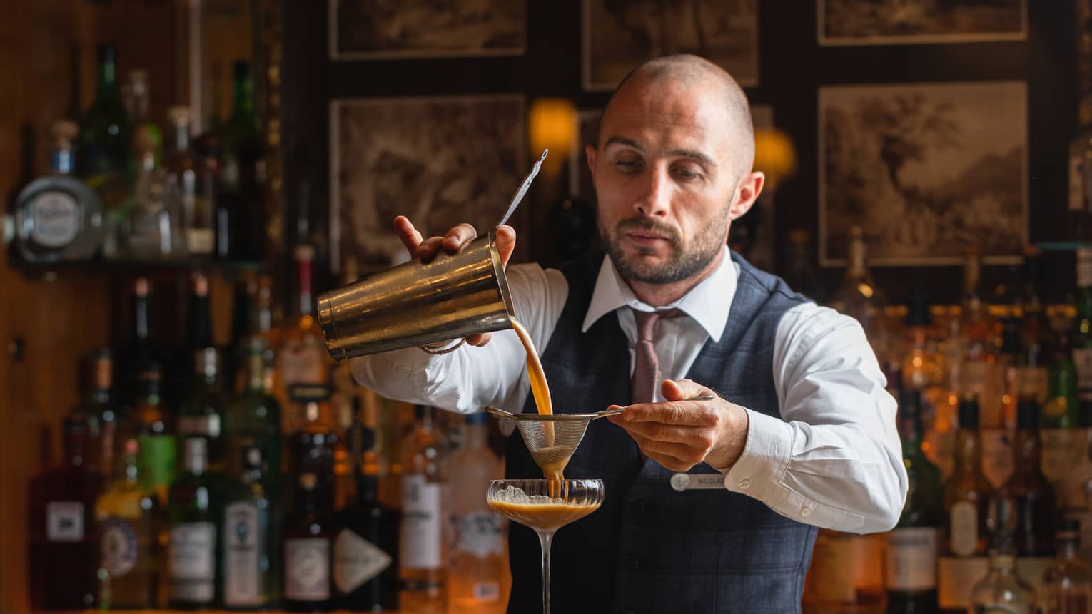 A bartender pouring a cocktail into a glass.