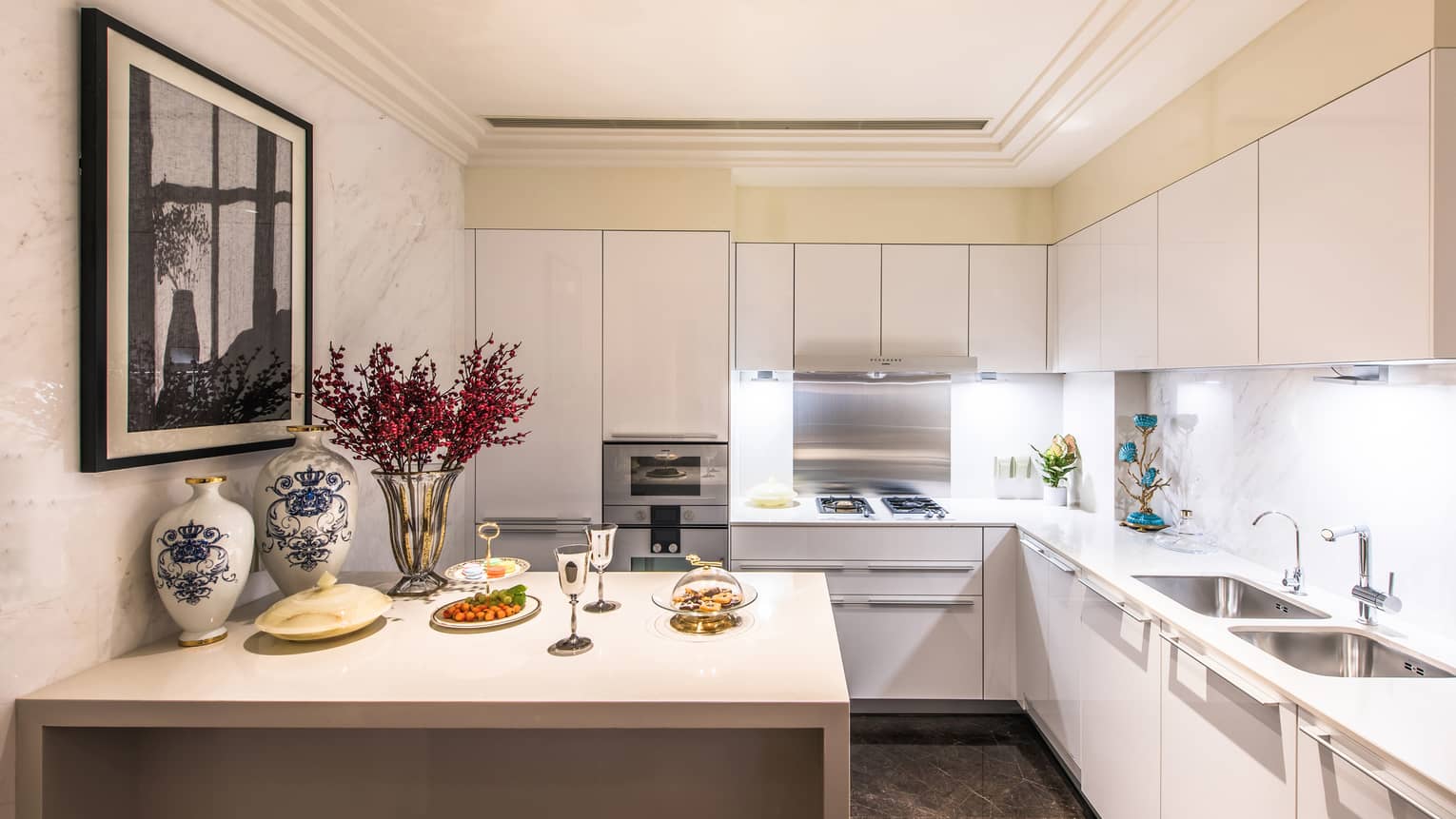 Kitchen with white cabinets, island counter with serving trays, wine glasses, vases and flowers