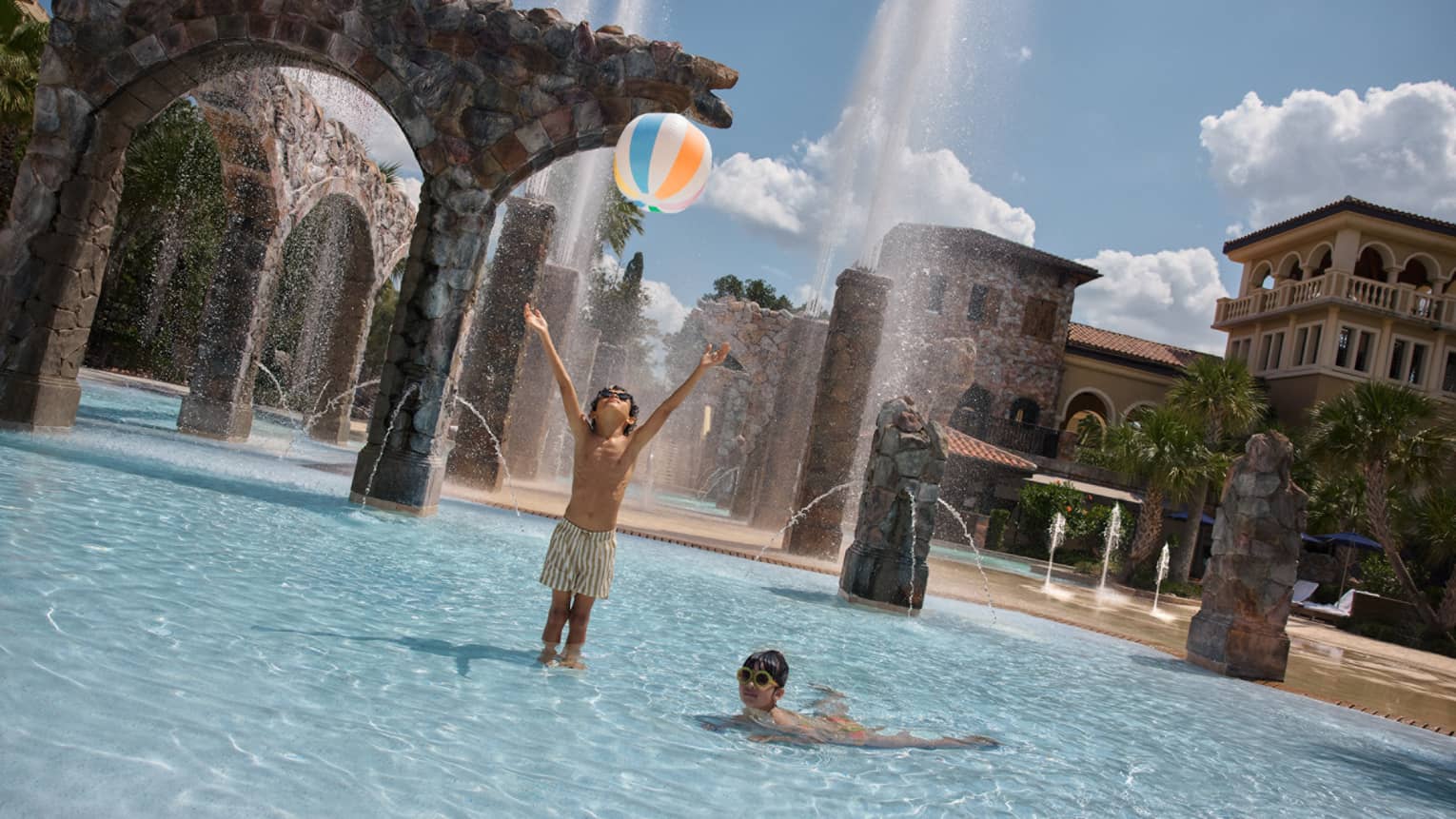 Two young guests wearing swimsuits and throwing a beach ball at the pool.