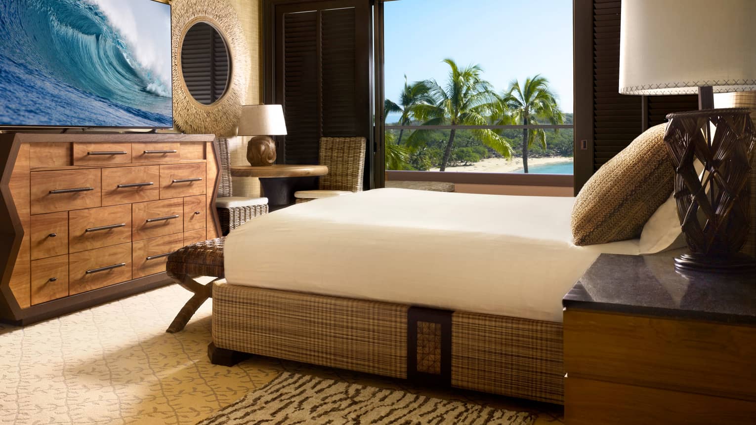 Penthouse Deluxe Suite bed with wicker frame in front of mid-century style dresser, TV displaying waves