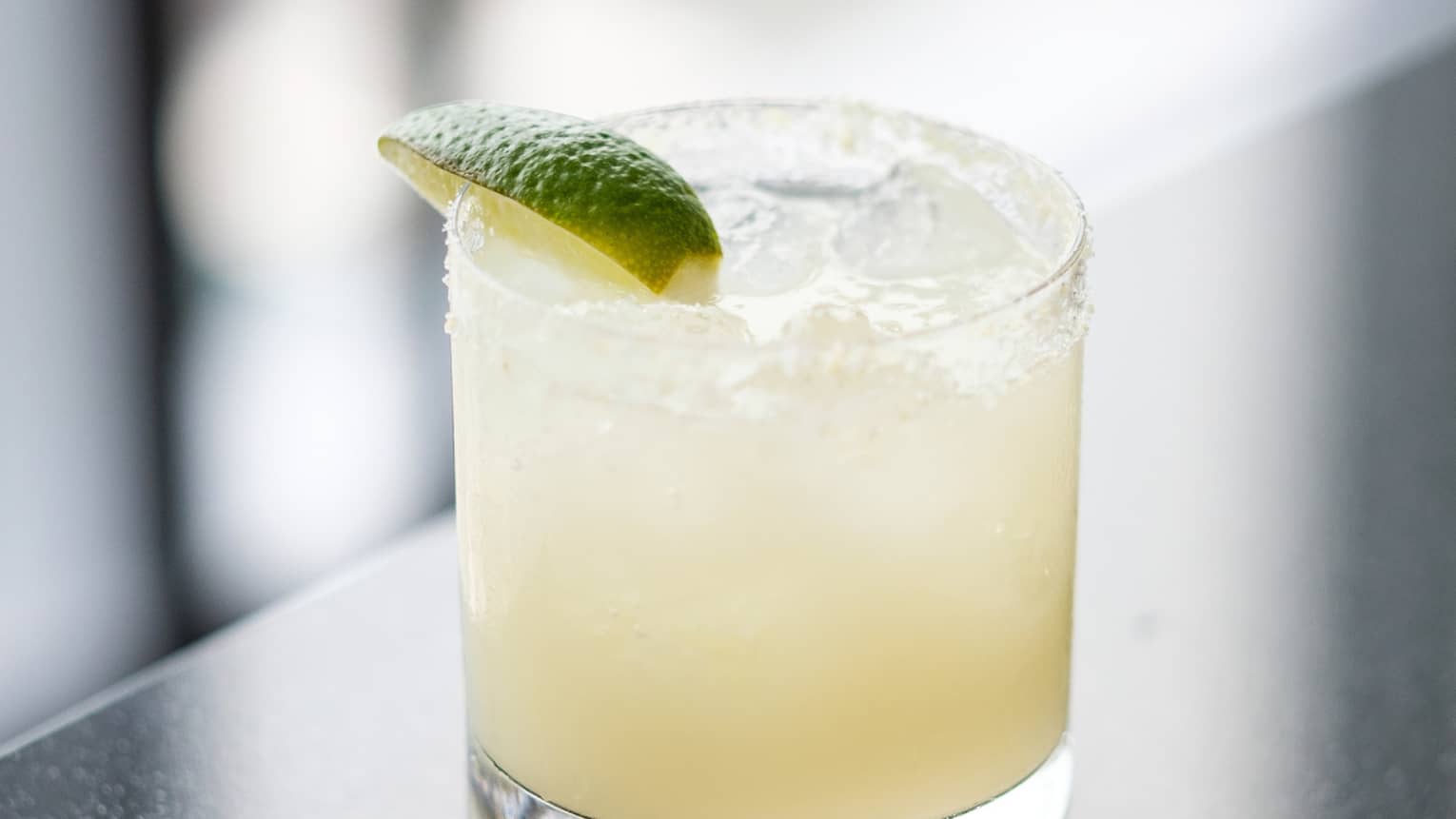 A light yellow coloured cocktail with a lime wedge.
