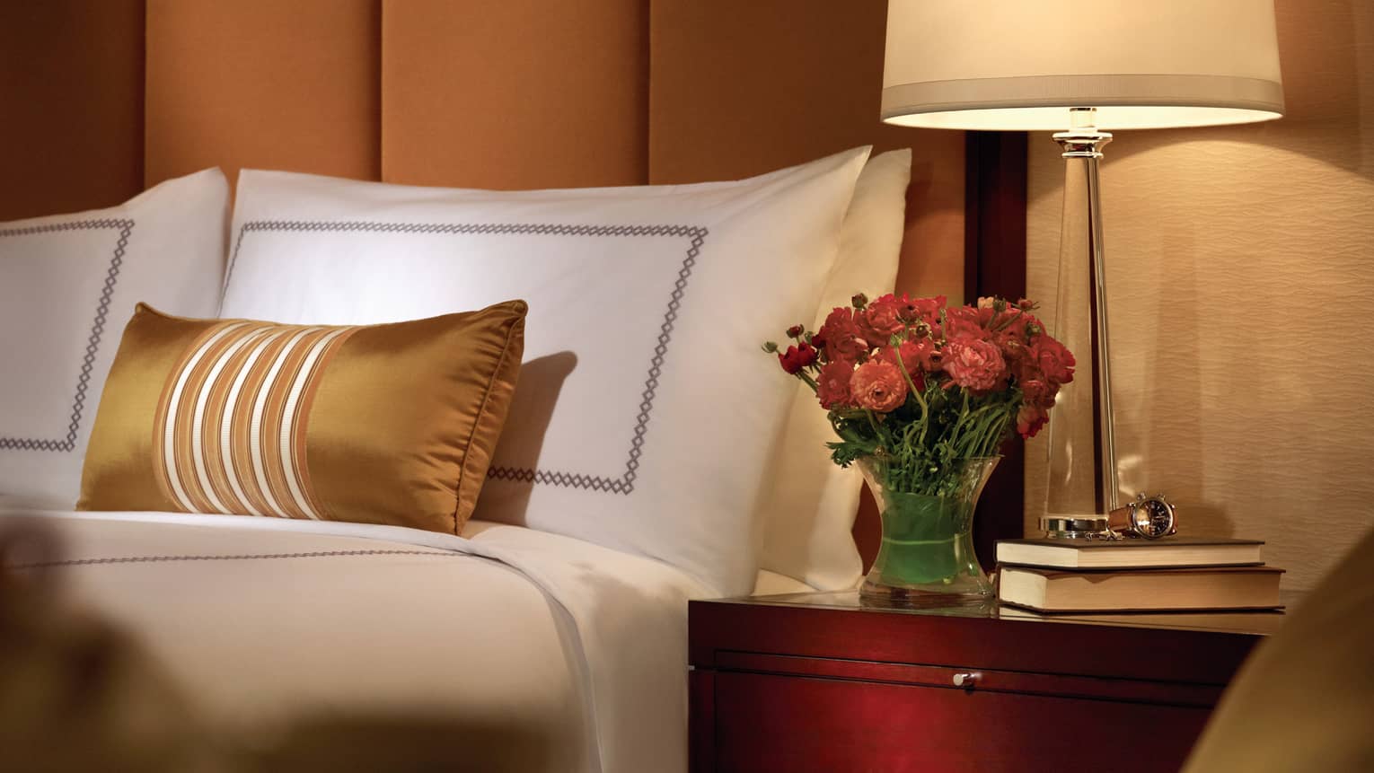 Premier Room close up of hotel room pillows, gold accent pillow, fresh pink flowers in vase on nightstand