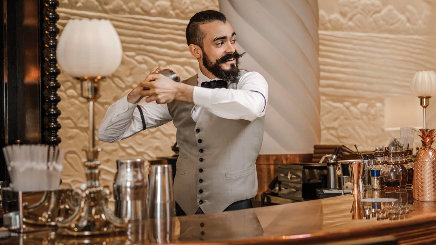 Mixologist with beard and waxed mustache, vest shakes cocktail behind bar