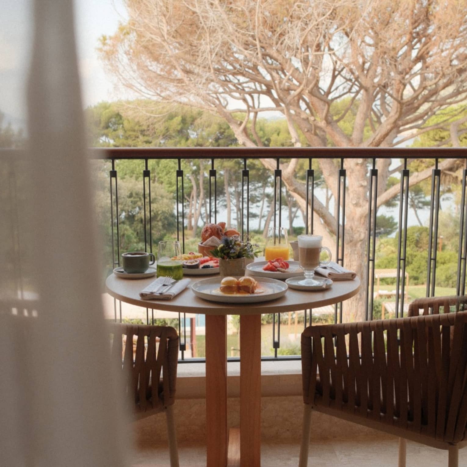 Breakfast dishes such as pastries, fruit, coffee and juice sit atop a table on a balcony overlooking lush greenery and water