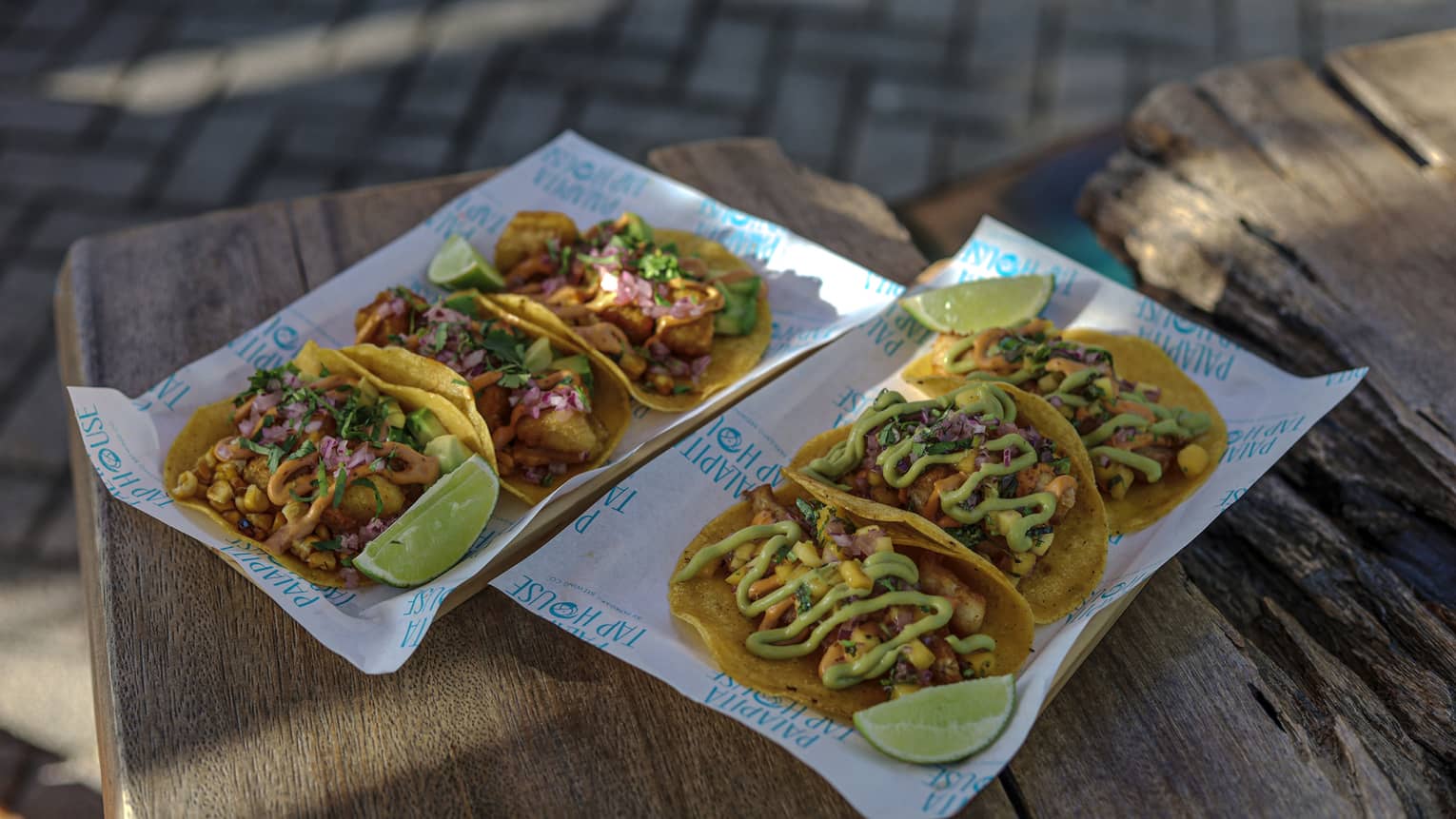 Six fish tacos plated in two rows of three with lemon wedges as garnish