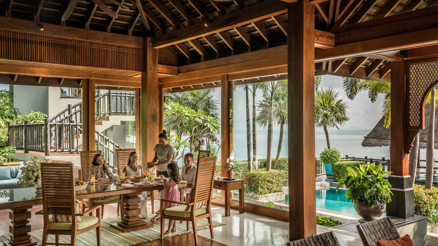 Butler serves family at long table in bright corner window dining room with windows
