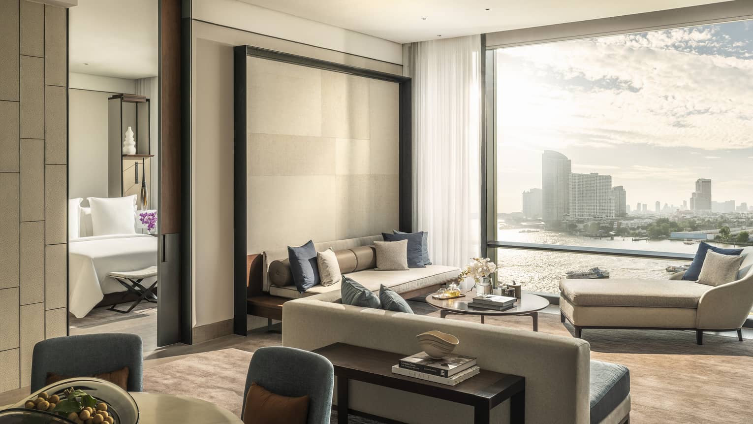 Hotel suite's living area with two sofas, chais lounge, wall of windows, connecting to bedroom