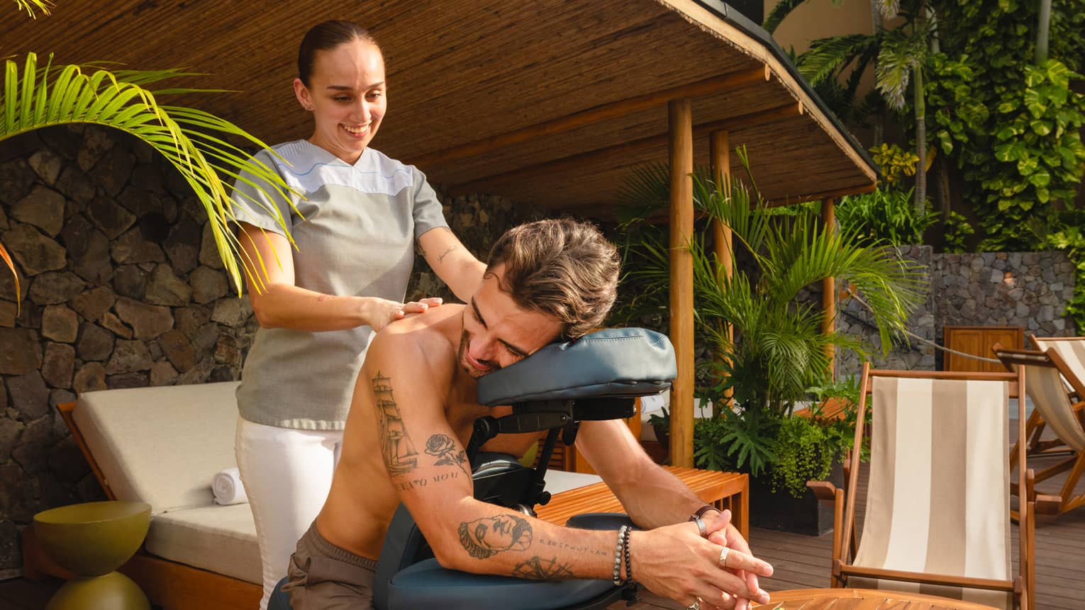 Massage therapist massages guests shoulders in a poolside cabana