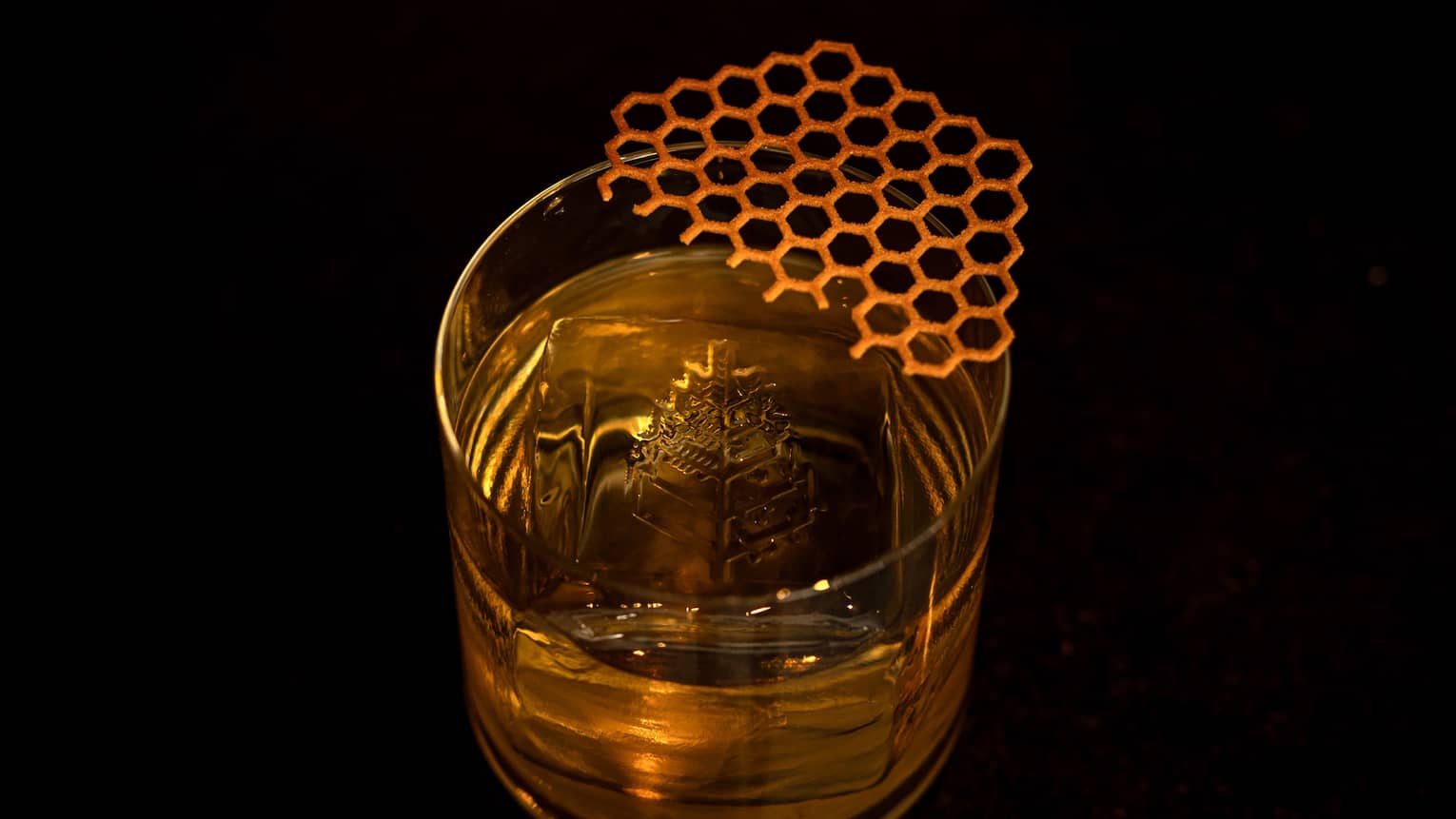 A clear tumbler contains a golden-hued cocktail, ice and garnish