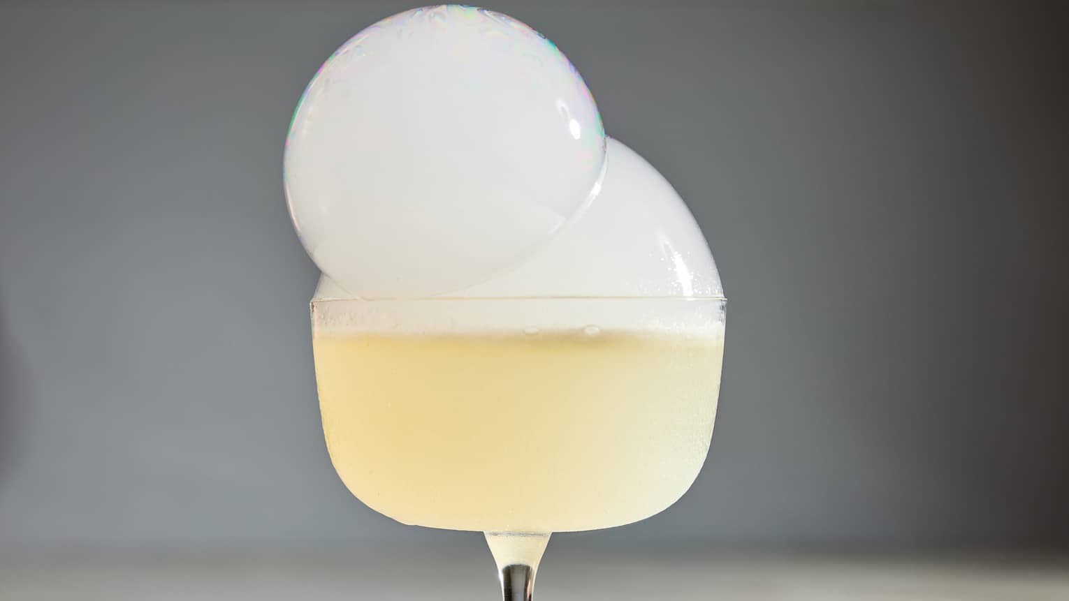 A glass of a yellow drink with bubbles on top.