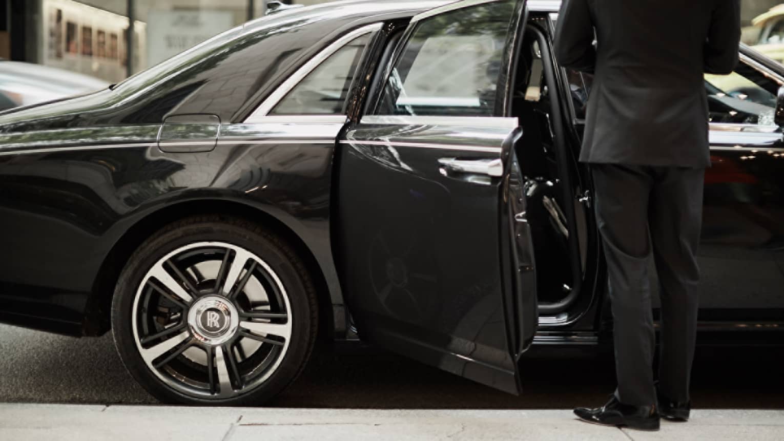 Man in suit by open door of black luxury car