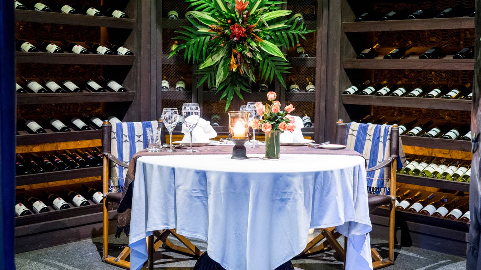Round dining table with white cloth set with wine glasses, flowers in wine cellar enclave