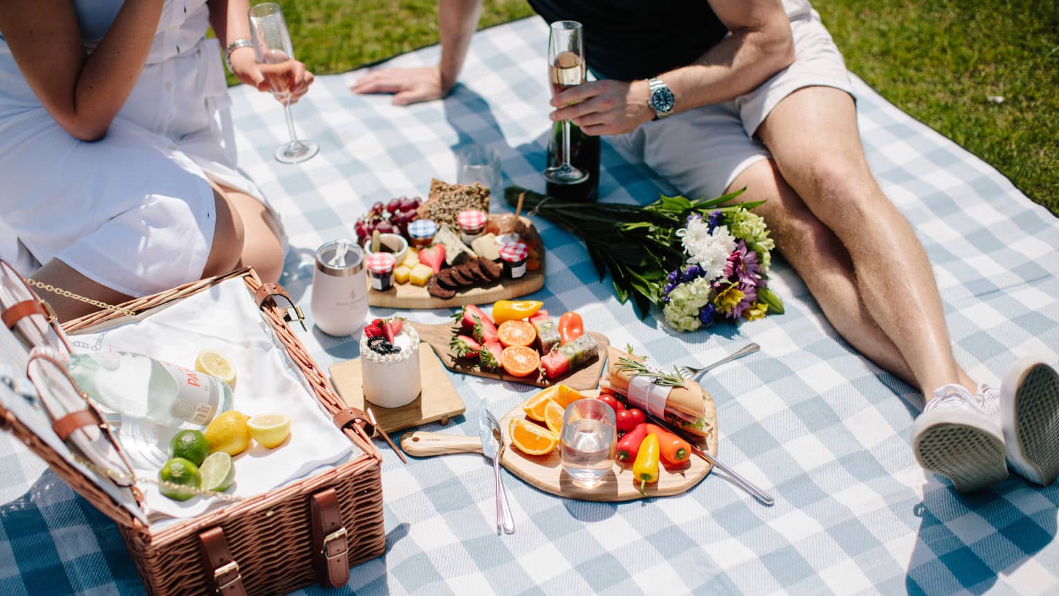 Two people enjoying a large picnic in a park during a sunny day.